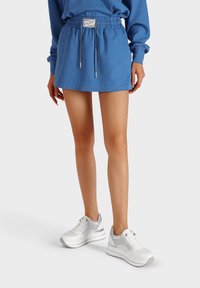 Abito felpa blu con vita elastica, cordino e patch con logo, abbinato a sneakers bianche chunky con accenti grigi e stringhe.