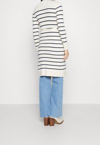 Krämfärgad ribbad klänning med marinblå ränder, bälte i midjan, kombinerad med ljusblå vida jeans och beige klackstövlar.