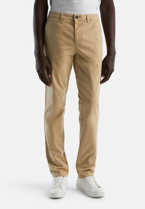 Beige chinos made of cotton blend fabric, featuring a button closure, front pockets, and a slim fit design, paired with white sneakers.