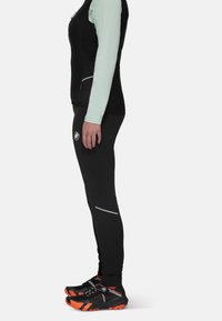 Sportieve outfit met een zwarte vest en zwarte broek met reflecterende accenten. Schoenen zijn zwart met oranje details en een vetersysteem.