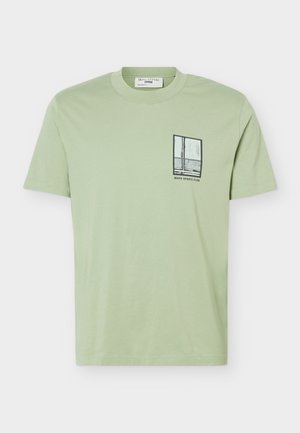 Hellgrünes T-Shirt mit kurzen Ärmeln und einer kleinen schwarz-weißen Grafik eines Fensters sowie dem Text "MOPD SPORTS CLUB" auf der linken Brustseite.