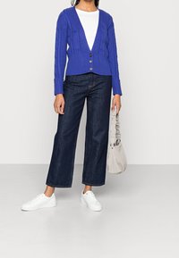 Blå ribbad cardigan med kabelstickad design, V-ringning och tre bruna knappar. Matchad med mörka denim byxor med vida ben och vita sneakers.