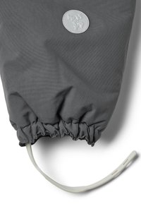 Harmaa kangaspussi, jossa on joustava aukko, harmaa pyöreä logotunniste ja valkoinen hihna, joka ulottuu pohjasta.