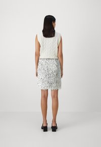 Haut en tricot crème à manches courtes, présentant un motif texturé ; jupe mini frangée argentée avec une finition brillante ; chaussures noires à talons carrés.