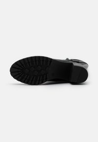 Černá gumová podešev s vzorem na podrážce, který obsahuje hluboké drážky a kulaté úchyty. Pevný podpatek a hladký design svrchní části.