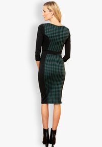 Abito a fantasia houndstooth nero e verde petrolio con maniche a tre quarti, silhouette aderente e lunghezza al ginocchio. Stivaletti neri alla caviglia completano il look.
