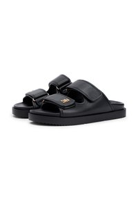 Μαύρα δερμάτινα σανδάλια τύπου slide με δύο ρυθμιζόμενους ιμάντες με χρυσές λεπτομέρειες και χοντρή, υφή μαύρη λαστιχένια σόλα.