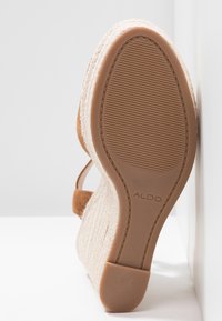 Sandale espadrille compensée avec semelle en caoutchouc texturée et nom de la marque ALDO visible sur la semelle, talon compensé tissé beige et bride en daim marron clair.