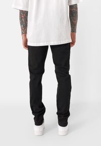 Czarne bawełniane spodnie o slim fit, w połączeniu z luźną białą koszulką i białymi trampkami, prezentując casualowy strój.