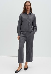 Chemise grise à boutons avec col et manches longues, associée à un pantalon gris assorti à jambes larges et des ballerines noires à bouts carrés.