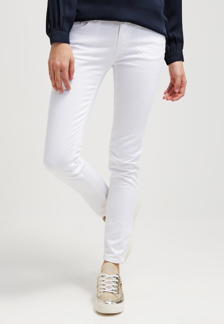 Vita smala jeans med en slät textur, framfickor och en midjehöjd som ligger mitt emellan, i kombination med ljusa sneakers med metalliska detaljer.