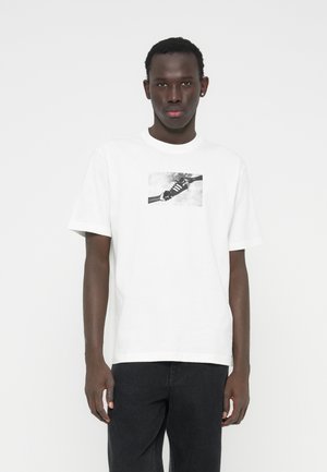 T-shirt branca de algodão com uma imagem gráfica a preto e branco de um ténis, mangas curtas, decote redondo e ajuste relaxado.