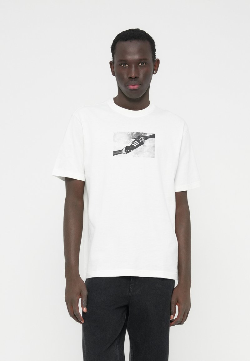 Biała bawełniana koszulka z krótkim rękawem, o okrągłym dekolcie i luźnym kroju, z czarno-białą grafiką sneakersa.