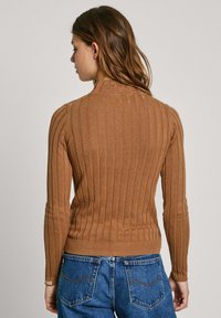 Brun ribbad tröja med hög krage och långa ärmar, tillverkad av ett mjukt material. Bärs med blå högmidjade jeans.
