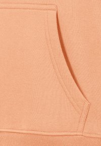 Pfirsichfarbene Sweatshirtstoff mit einer Kängurutasche, geripptem Saum und Nähdetails, die eine weiche, strukturierte Oberfläche präsentieren.