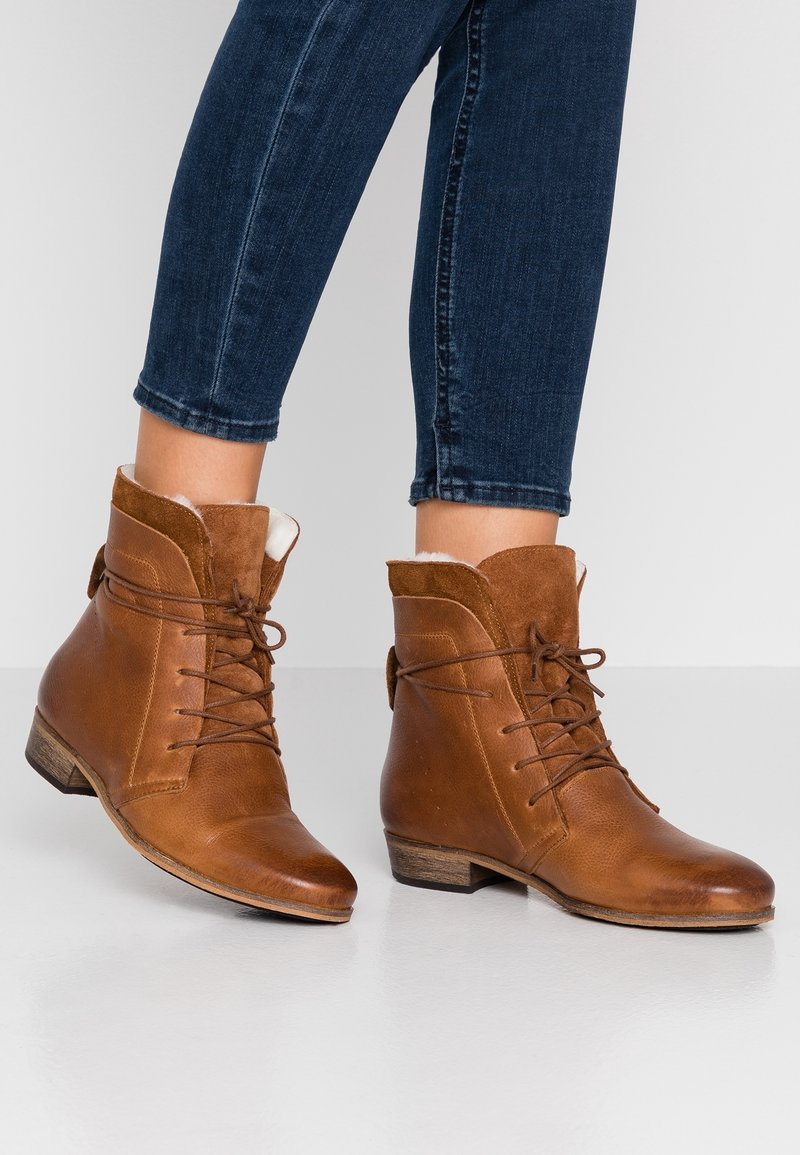 Bottines en cuir marron à lacets, avec un dessus en daim, dotées d'un col rembourré et d'un petit talon empilé. Texture lisse et détails minimaux.