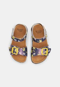 Mitmevärvilised sandaalid, millel on tumesinise taustaga kollased palmid ja ankruid, laia rihmaga, millel on kollane pandla ja pruun sisetald.