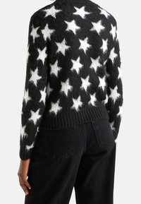 Svartvit stjärnmönstrad tröja med en fluffig textur, med ribbad fåll och långa ärmar, kombinerad med mörka jeans.