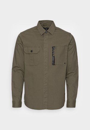 Khaki grøn langærmet skjorte med to brystlommer foran, den ene med klap og knap, den anden med en lodret lynlås.