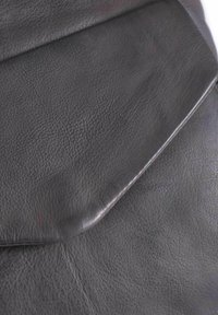 Materiale in pelle nera con superficie texture. Presenta una chiusura a patta liscia e curva e cuciture visibili lungo i bordi.