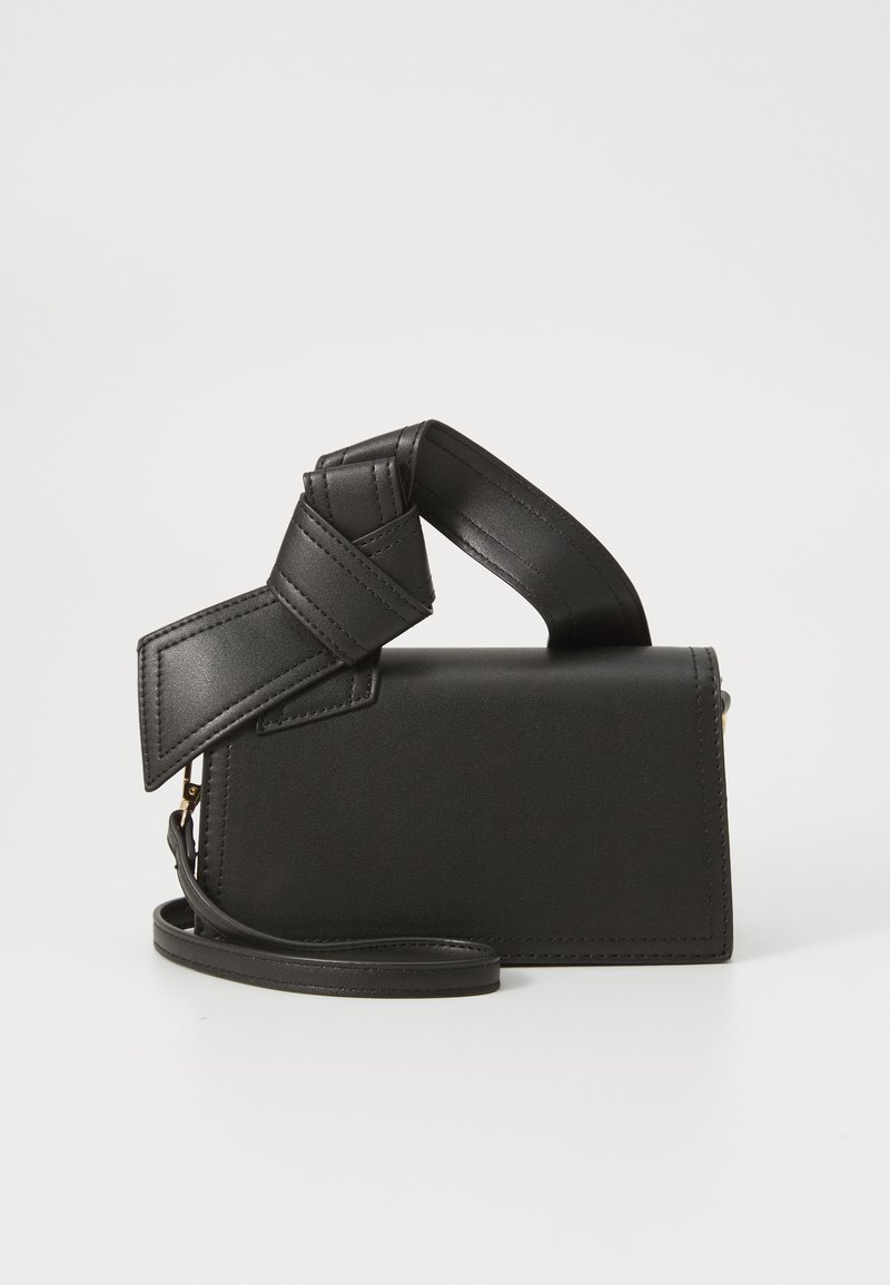 Bolso de cuero negro con forma rectangular, que presenta un asa anudada única y una correa de hombro desmontable. Textura suave y costuras mínimas.