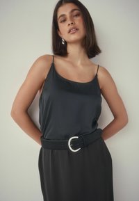 Czarna satynowa koszulka na ramiączkach z cienkimi ramiączkami, zestawiona z pasującą spódnicą z szerokim czarnym paskiem i srebrnym detalem z klamrą.
