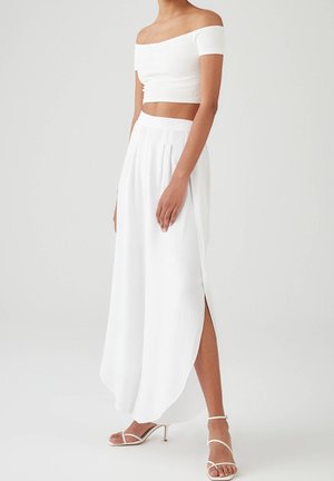 Vit off-shoulder crop top matchat med en lång vit plisserad kjol med en sidslits, slät textur och sandaler med hög klack och remmar.