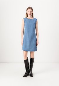 Denim kleita ar taisnu griezumu, apaļu kakla izgriezumu un bezpiedurkņu dizainu. Atvērts apakšmalā un zila auduma kombinācija ar melniem augstiem zābakiem.