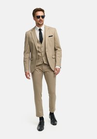 Beige Dreiteiler mit slim fit, ausgestattet mit einem Reverskragen, schwarzer Krawatte und Einstecktuch. Schwarze Dresschuhe runden den Look ab.