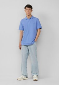 Jasnoniebieska koszulka polo z kołnierzykiem i krótkimi rękawami, w połączeniu z jasnoniebieskimi dżinsami o luźnym kroju oraz białymi sneakerami z beżowymi akcentami.