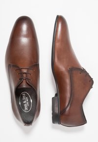 Een paar bruine leren veterschoenen voor mannen, waarvan de ene een bovenzijde laat zien en de andere een zijaanzicht, op een witte achtergrond.