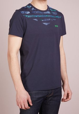 Navy blue short-sleeve T-shirt with blue-green geometric pattern across chest and "BOSS" logo, worn with dark denim jeans.