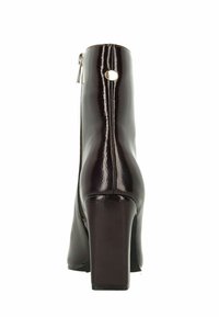 Bottine en cuir verni noir avec un talon carré, fermeture éclair sur le côté et un détail en découpe circulaire à l'arrière. Texture lisse et design épuré.