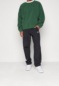 Zelená fleecová mikina s černým logem, ve spojení s černými cargo kalhotami s kapsami. Bílé tenisky doplňují celý outfit.