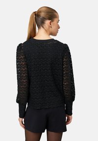 Fekete texturált blúz áttetsző, puffadt ujjakkal és kerek nyakkivágással. A szegély hullámos, bonyolult mintázatú anyagból készült.