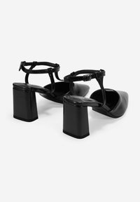 Zapatos de tacón bloque de cuero negro con tira en el tobillo. Presentan una punta afilada y una textura suave. Hebilla ajustable.