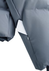 Siva puffer jakna s glatkom, mat površinom, detaljima u obliku zatvorenih džepova i oznakom koja viri iz šava.