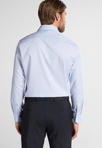Camicia a maniche lunghe a righe blu chiaro con colletto a punta, texture liscia e polsini abbottonati, abbinata a pantaloni scuri e una cintura coordinata.