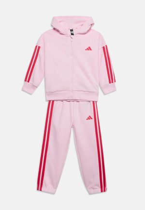 Hellrosa Kinder-Zip-Hoodie und Hose mit roten Streifen an Ärmeln und Beinen und kleinem roten Logo auf Brust und Oberschenkel.