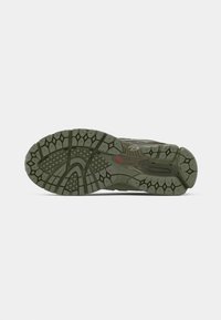 Semelle de chaussure de randonnée verte avec un caoutchouc texturé pour l'adhérence, présentant un motif de bande de roulement géométrique et une touche de rouge sur le côté.