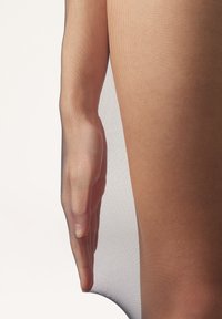 Przezroczyste, cieliste rajstopy częściowo zakrywające dłoń. Tekstura jest gładka i przezroczysta, z delikatnym, drobnym siateczkowym wyglądem.