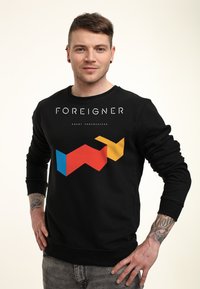 Felpa nera con stampa grafica in rosso, blu, giallo e bianco con il testo "FOREIGNER" e "AGENT PROVOCATEUR." Maniche con polsini a costine.