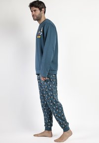 Pijamas de algodón en color verde azulado que incluyen una camiseta de manga larga con un gráfico de un personaje de dibujos animados y pantalones con un patrón que repite los diseños del personaje.