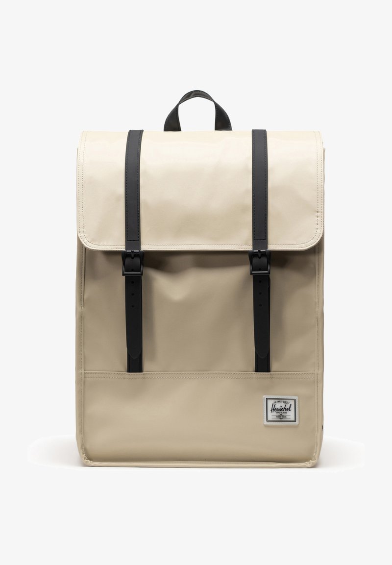 Beige ryggsäck med en strukturerad design, svarta justerbara remmar, klaffstängning och en framficka. Har en märkesetikett längst ner.