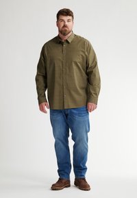 Camicia a maniche lunghe verde a fantasia con chiusura a bottoni, abbinata a jeans blu e stivali marroni; presenta una vestibilità comoda e un design con colletto.