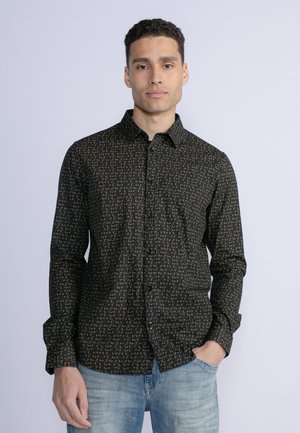 Camicia nera con bottoni, decorata con un modello geometrico giallo, dotata di colletto, maniche lunghe e una singola tasca sul petto. Indossata con jeans di denim chiaro.