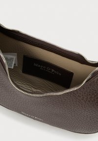 Pungă maro din piele texturată cu fermoar argintiu deschis, căptușeală interioară bej și etichetă neagră cu inscripția „Marc O'Polo” în interior.