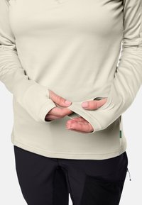 Lichtbeige langwerpige shirt met duimopeningen en een gladde textuur. De zoom is recht en de stof heeft een zachte, getailleerde uitstraling.