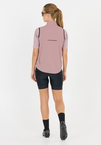 Helles rosa Fahrradvester mit kurzen Ärmeln, schwarzen Akzenten und einer reflektierenden Gesäßtasche, kombiniert mit schwarzen Fahrradhosen und Schuhen.