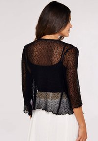 Cardigan negro ligero de punto con mangas de tres cuartos, dobladillo ondulado y una textura translúcida, superpuesto sobre una blusa lisa.